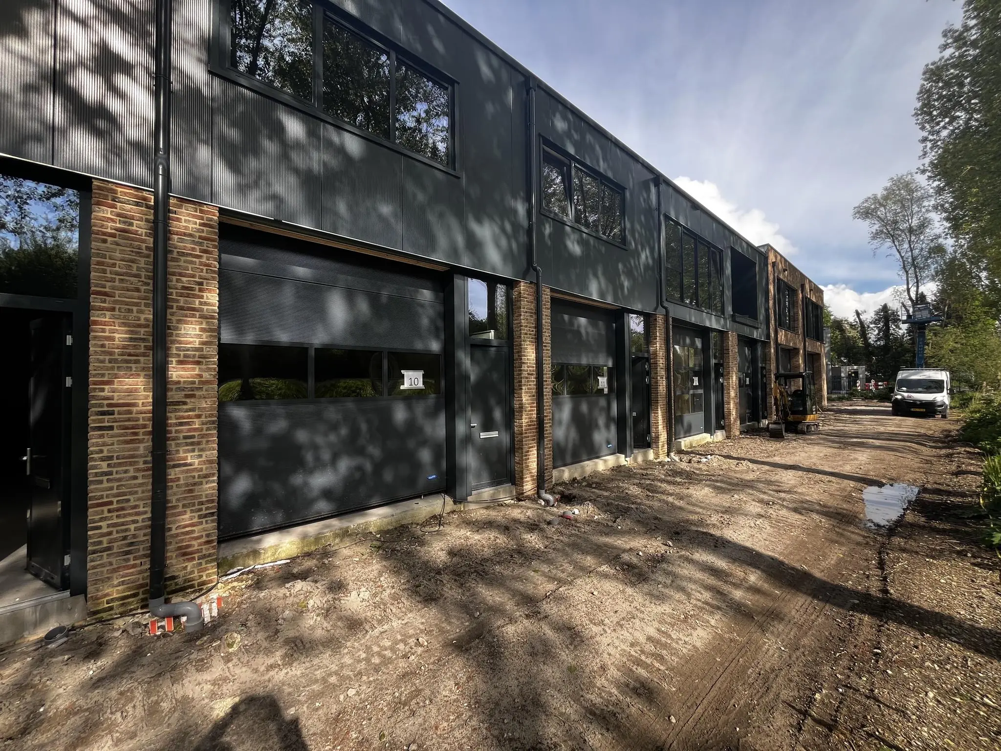 Nieuwbouw van moderne bedrijfsunits aan de Broekdijk West 19-10, met rolluiken en een onverharde toegangsweg.